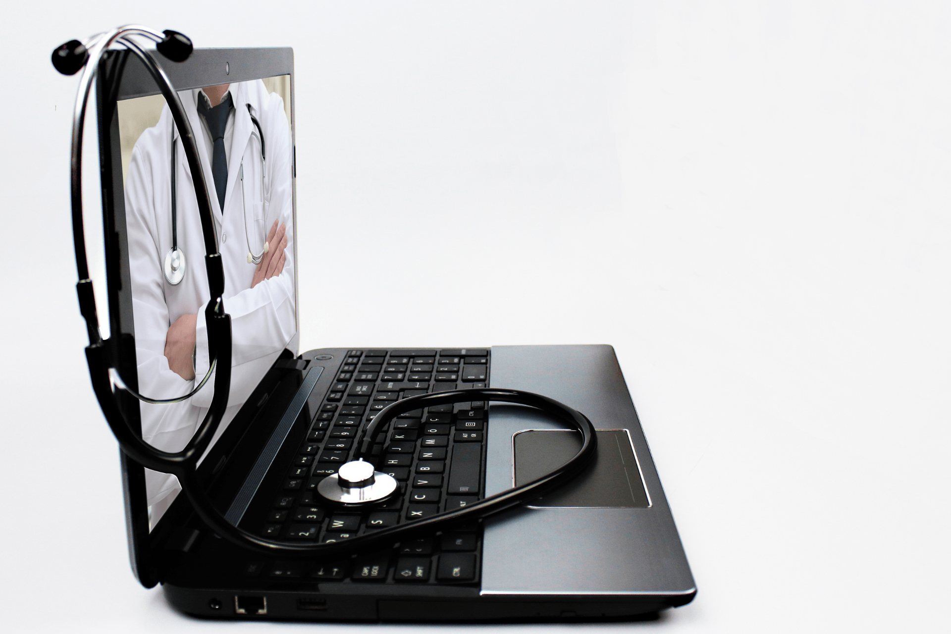 Stethoscope resting on a laptop keyboard showing a doctor on the screen.