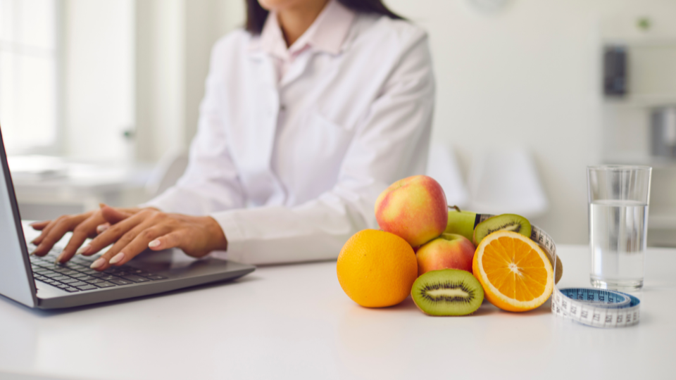 Dietitian with fruits and glass of water next to her while using laptop