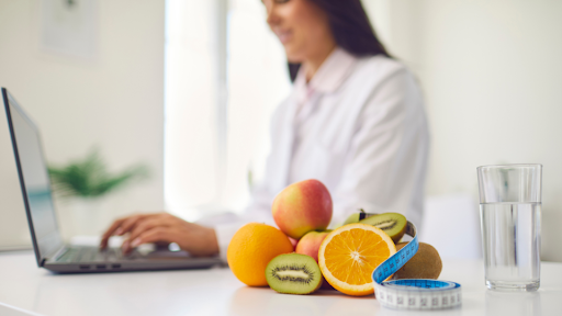 Fruits and a tape measure in front of a woman using her laptop