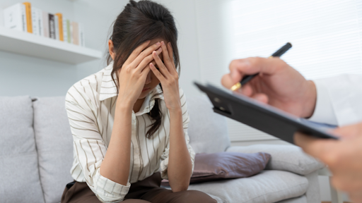 Woman with hands on forehead covering face in session with a therapist
