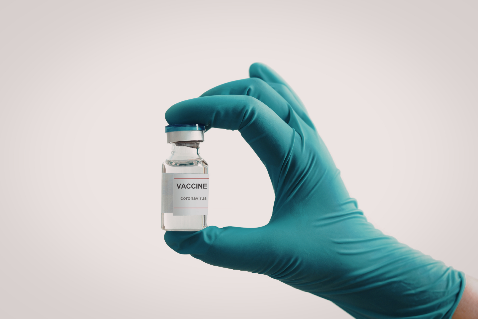 Gloved hand holding a small vial labeled vaccine