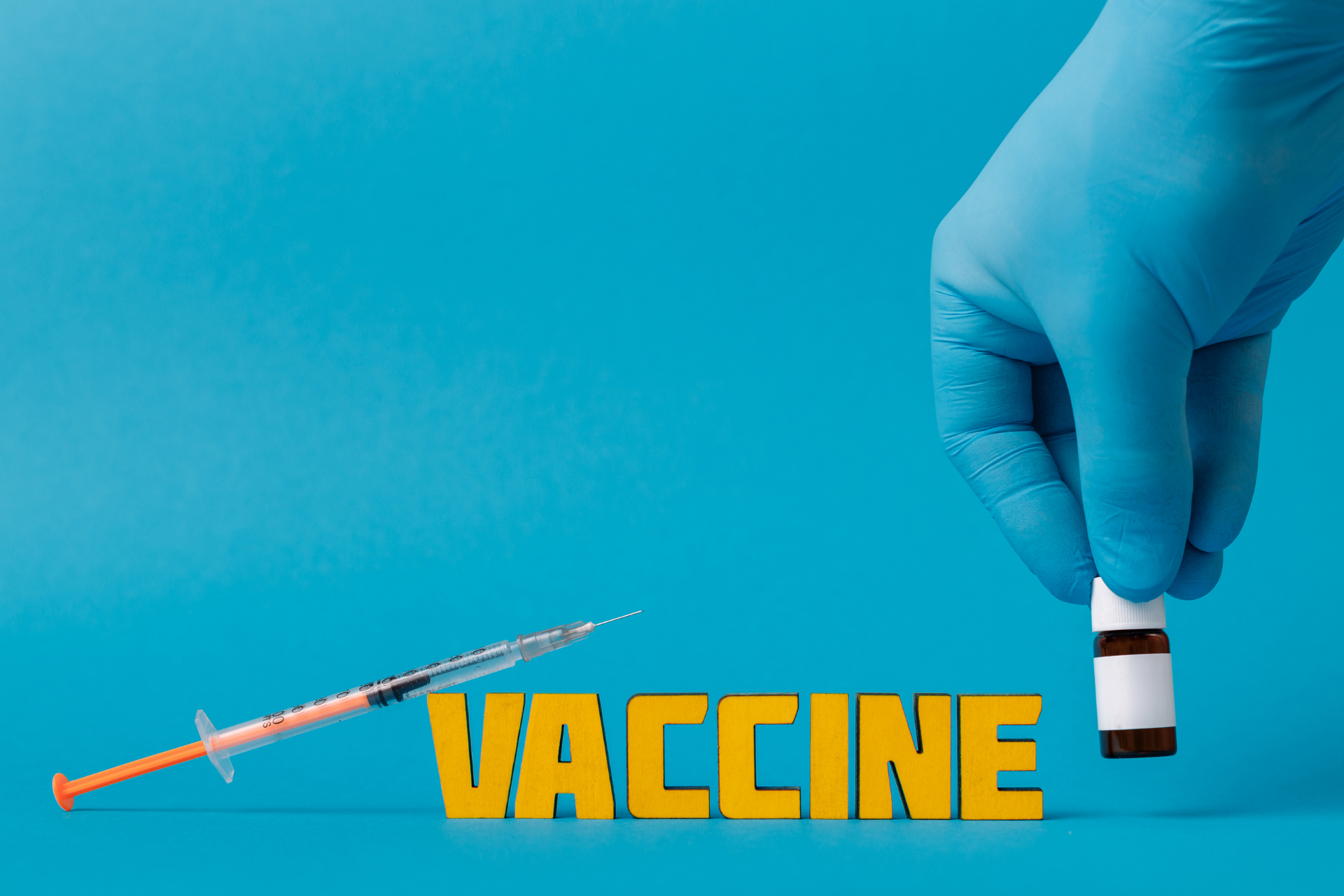 Gloved hand holding a vaccine vial next to a syringe and the word “vaccine"