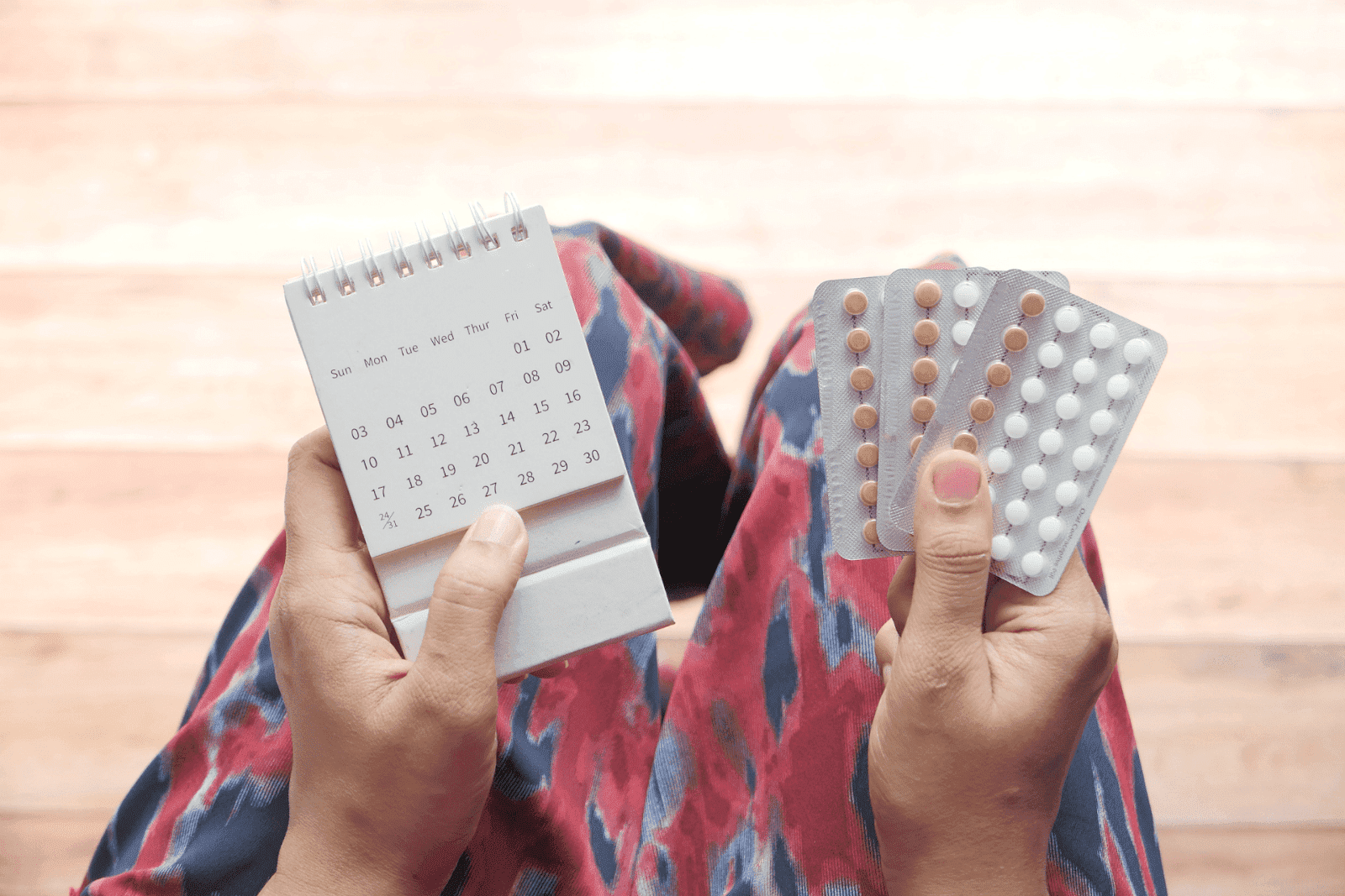 Hands holding a small calendar and blister packs of birth control pills, suggesting a medication schedule.  Other Foods