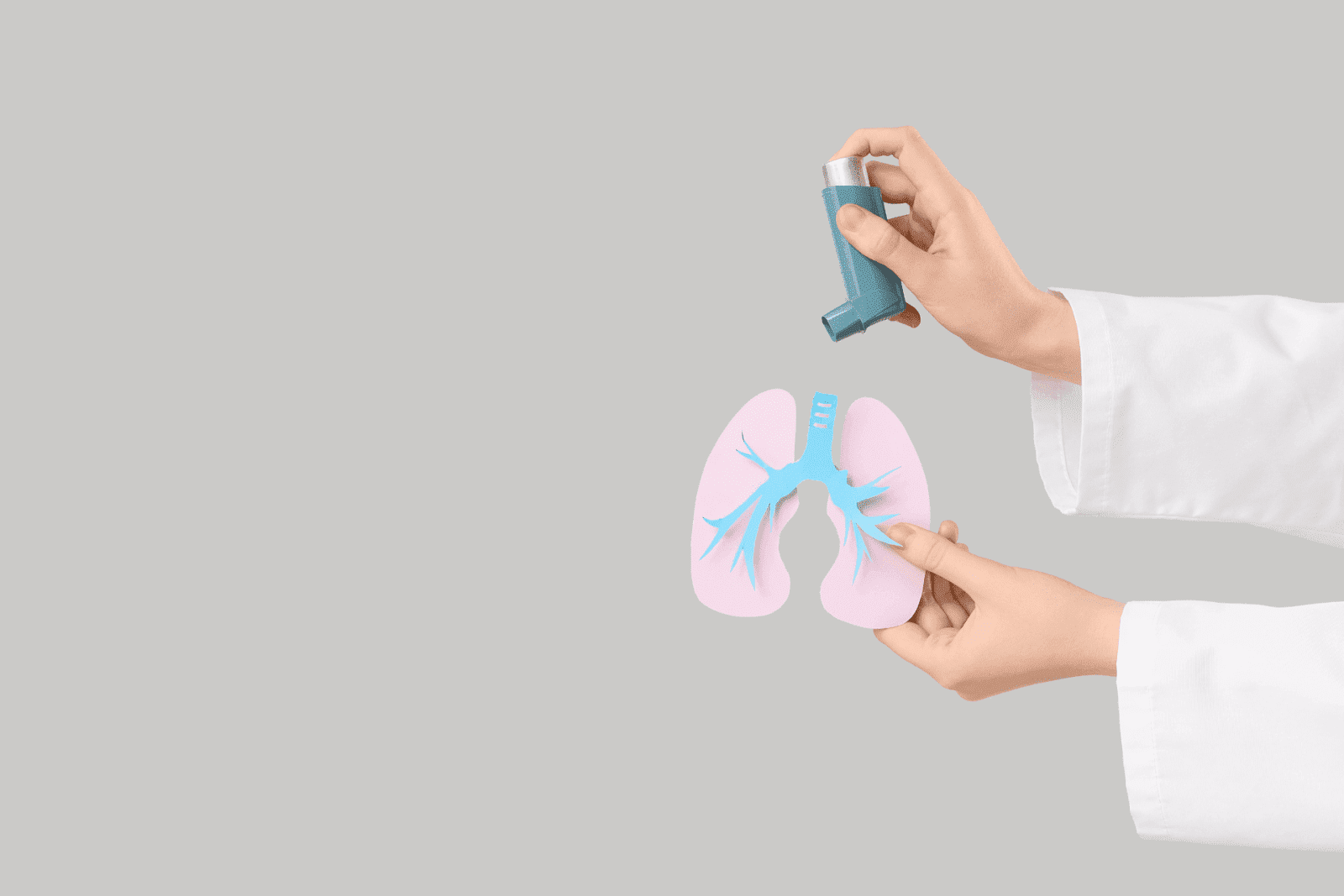 Hands holding an inhaler and a paper-cutout lungs illustration on a gray background