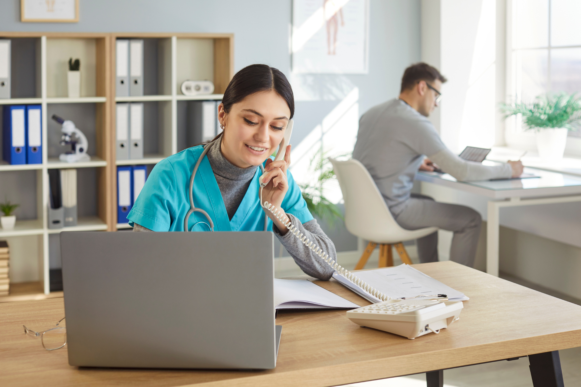 Healthcare professional speaking on the phone while working at a desk with a laptop