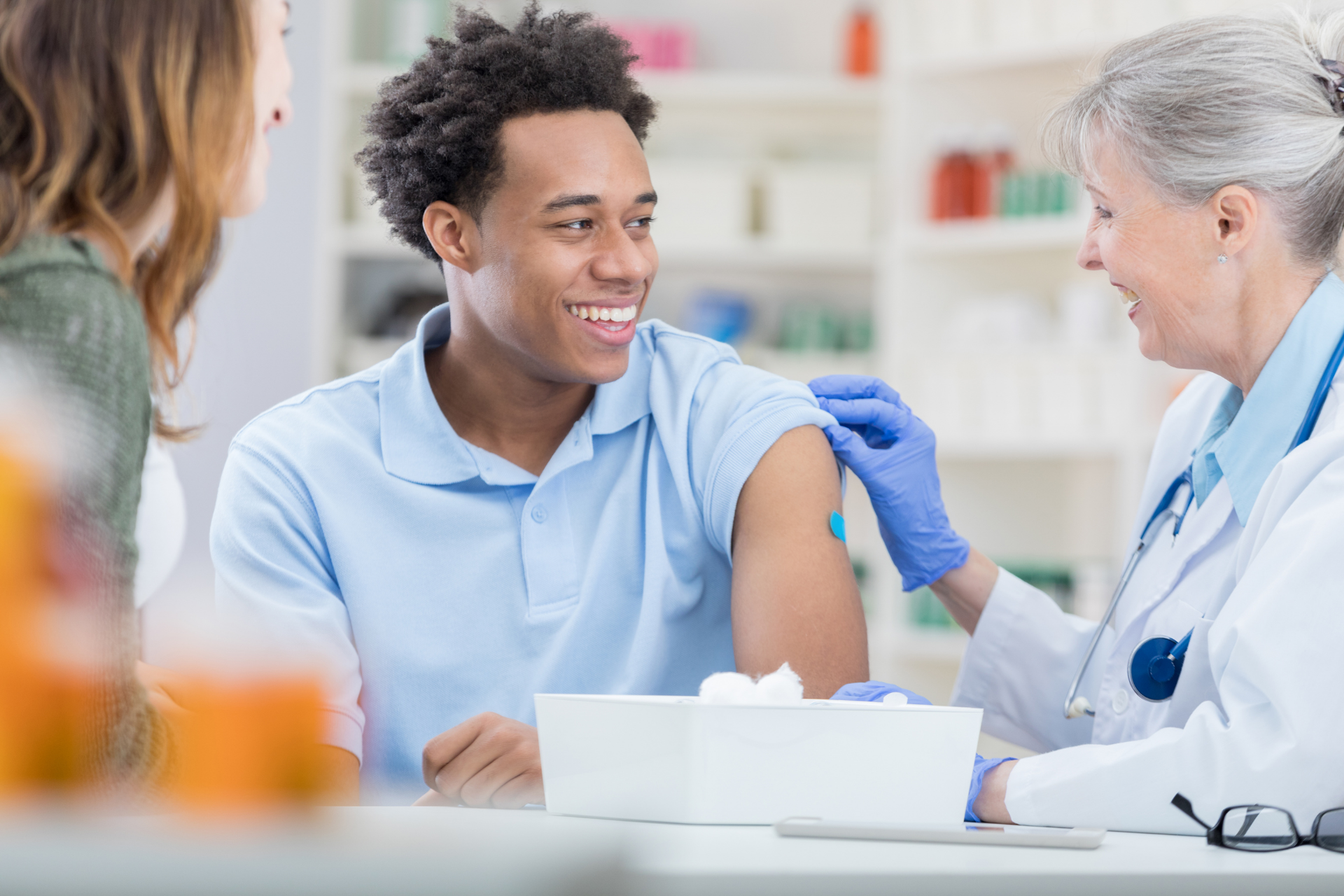 Healthcare worker applying a bandage after an injection while a smiling young man looks on