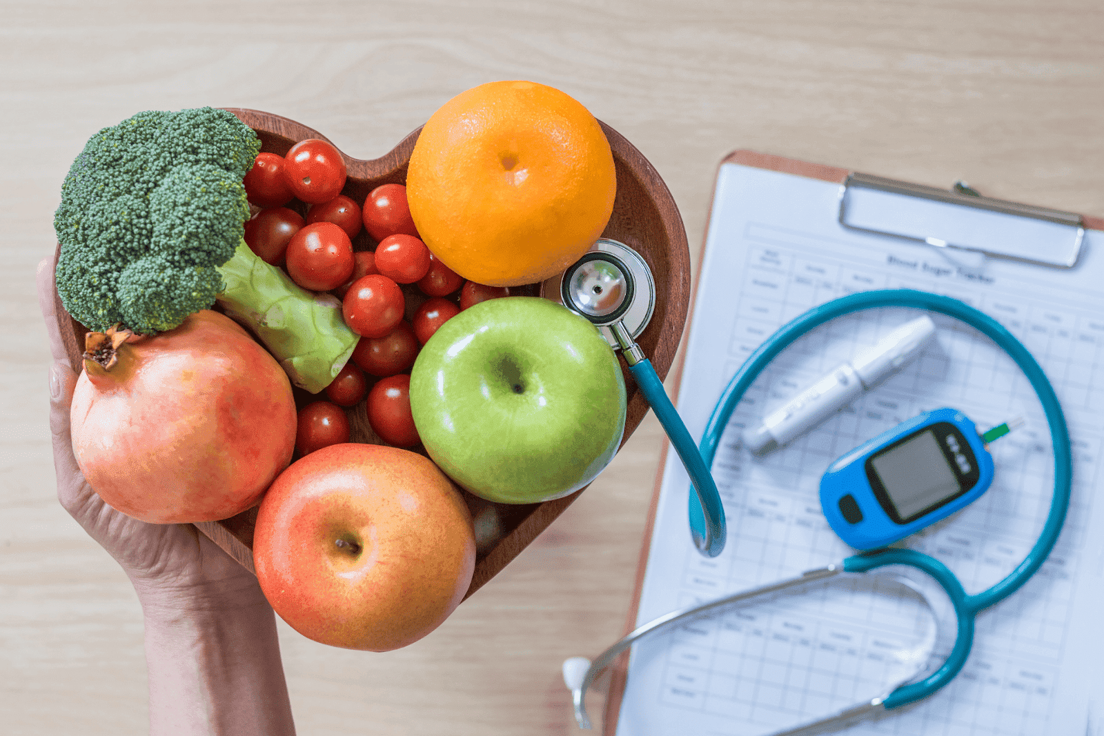 Heart-shaped bowl of fruits and vegetables next to a stethoscope and glucose monitor