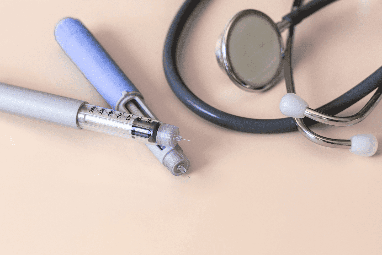 Insulin pens and a stethoscope on a light beige surface