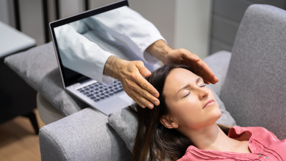 Creative image showing hands and part of arms coming out of laptop to be on each side of head of a woman laying down on couch.