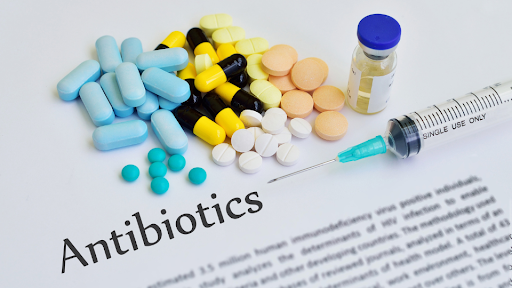 Multiple types of antibiotics and a syringe on top of a paper with "Antibiotics" as the heading.