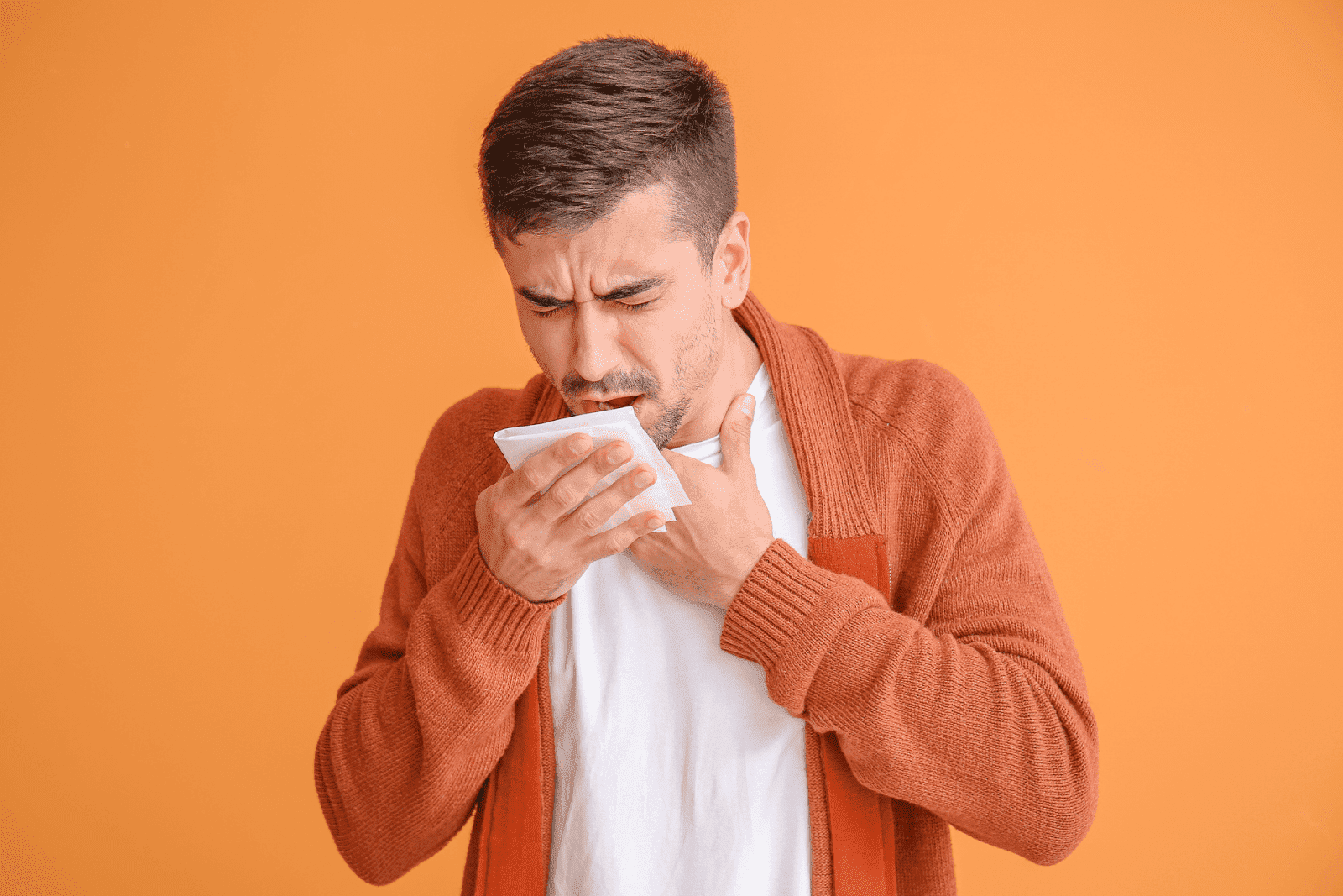 Man coughing into a tissue with a hand on throat.