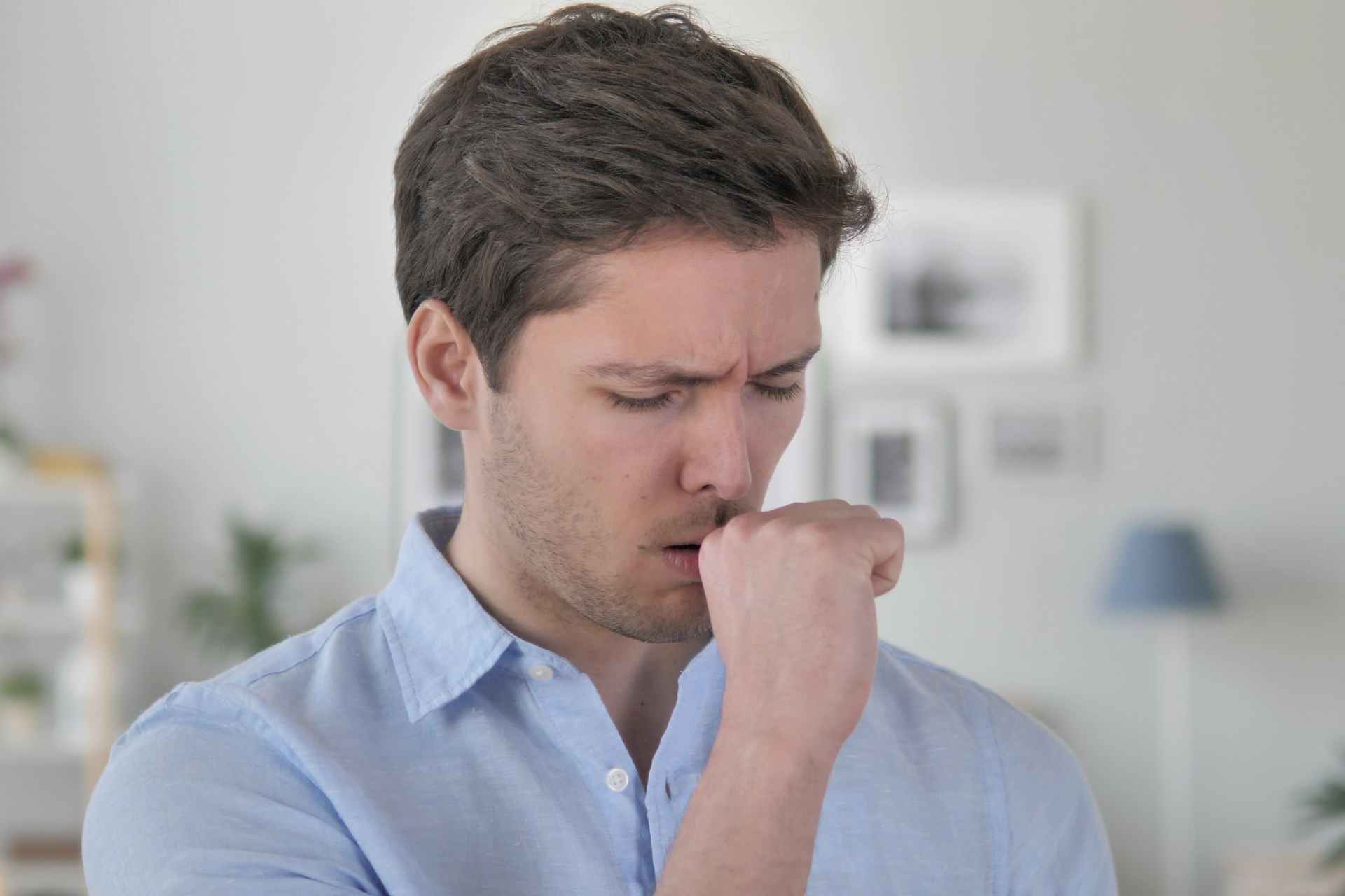Man coughing into his fist while standing indoors