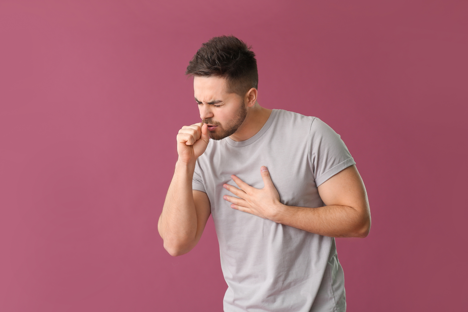Man coughing with hand on chest against a pink background