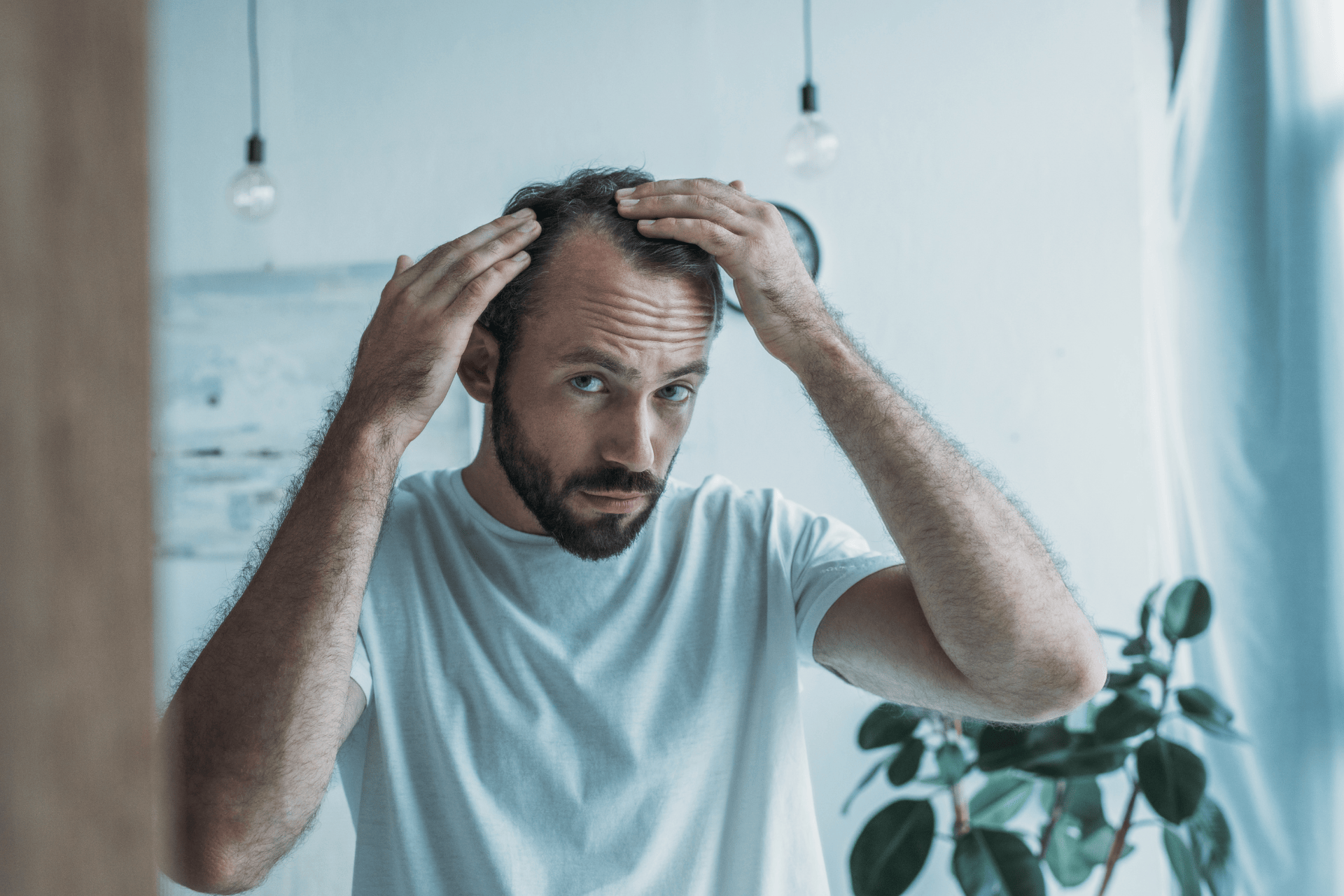 Man examining his thinning hair while looking in a mirror.