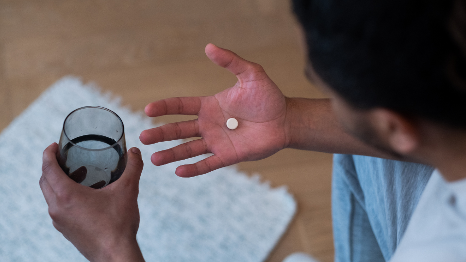 Man holding water in one hand and a pill in the other