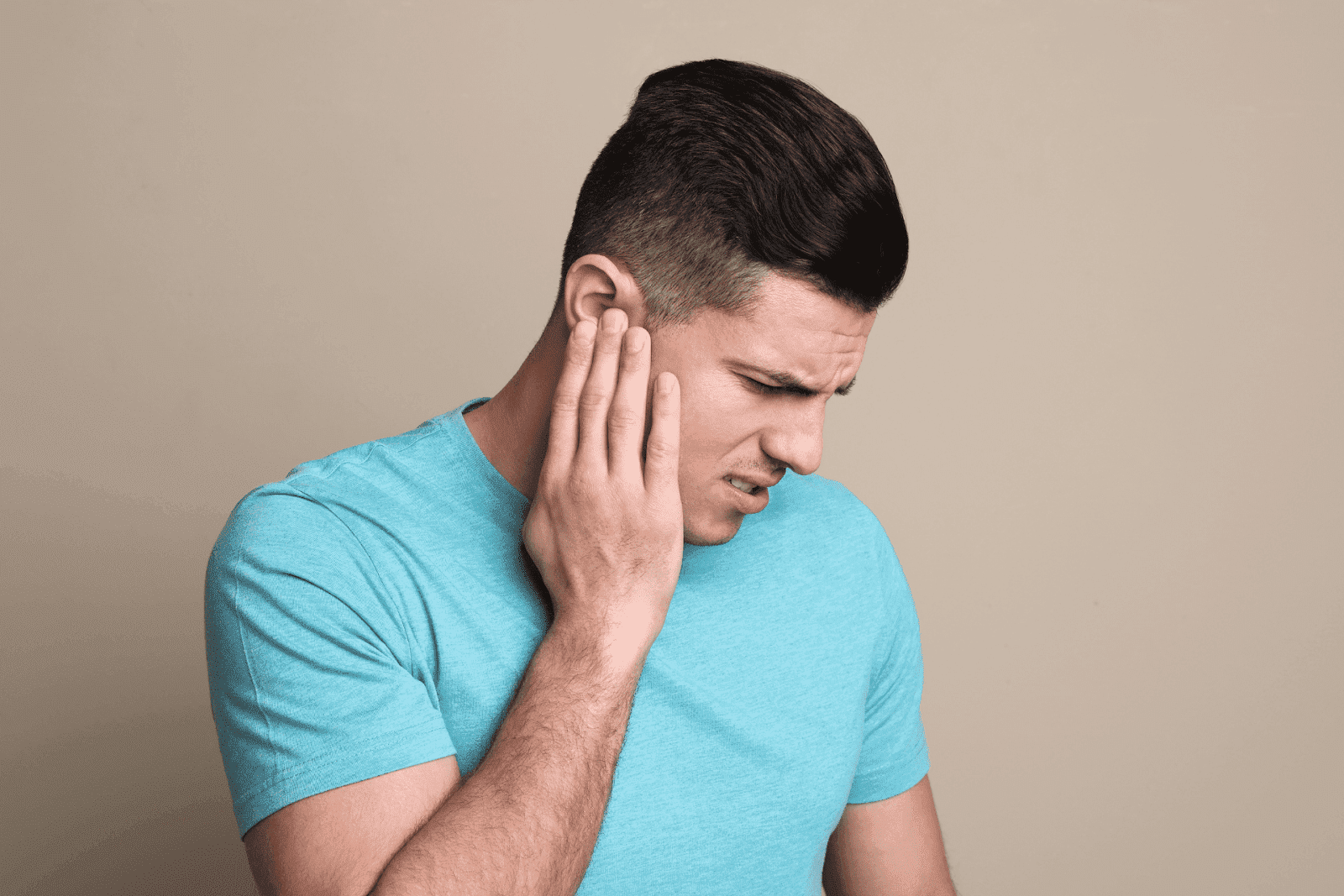 Man in a blue shirt holding his ear and wincing in pain