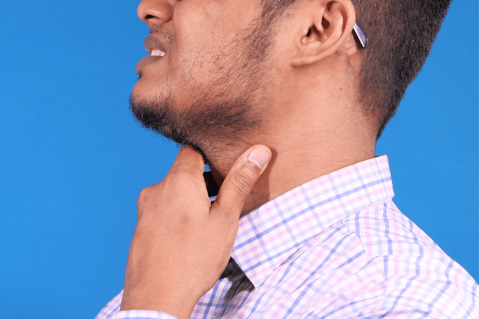 Man in a checkered shirt touching a lump on his throat with a concerned expression.