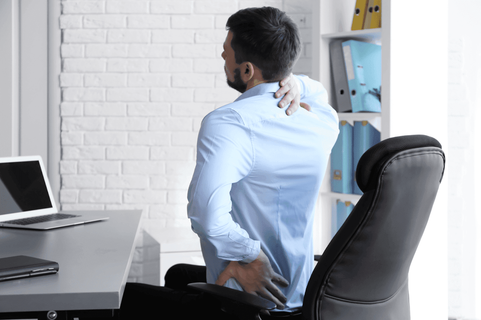 Man in office holding neck and lower back in pain while sitting at desk.