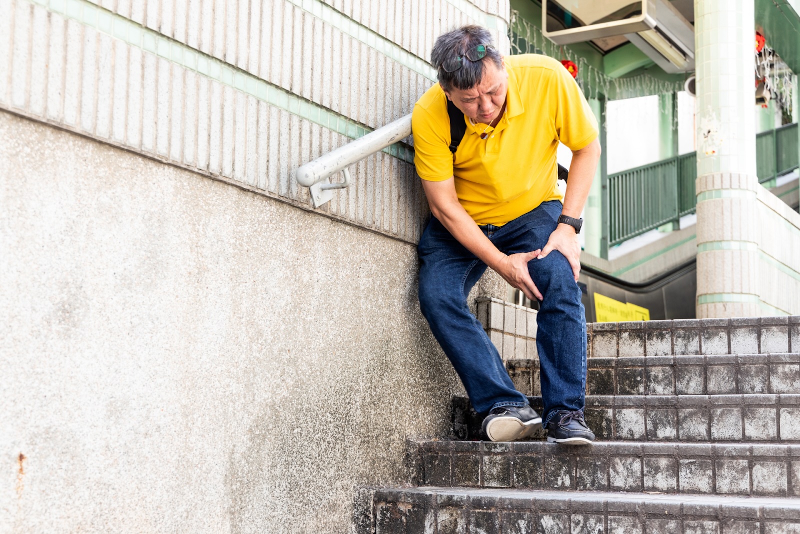 Man in yellow shirt holding his knee in pain on stairs.