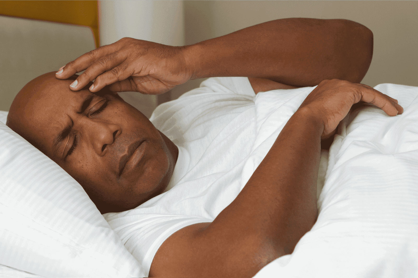 Man lying in bed holding forehead in discomfort.