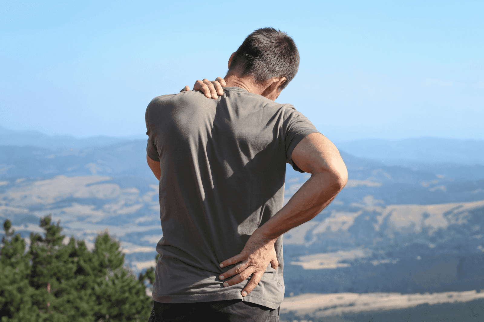 Man outdoors holding his neck and back in pain.