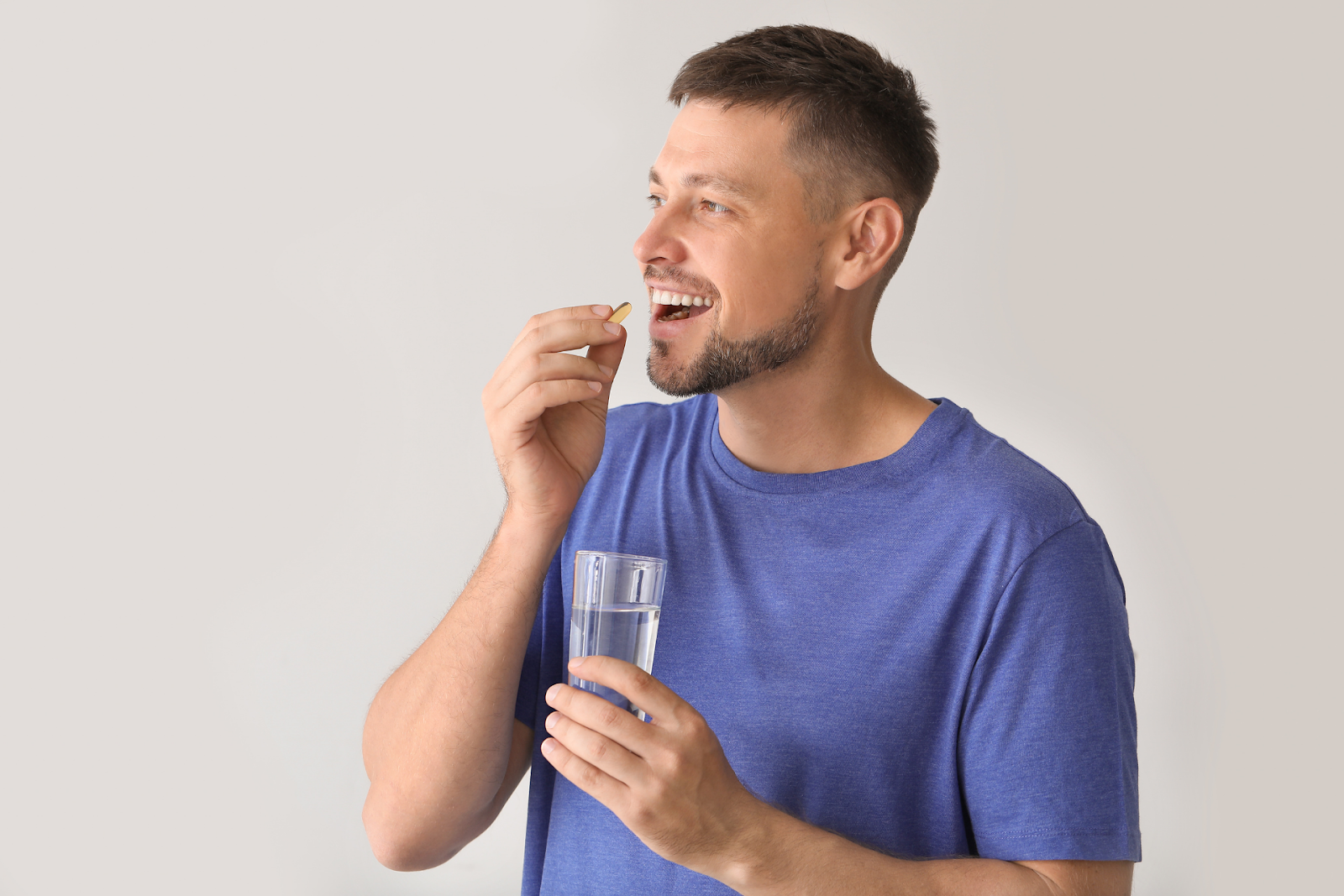 Man smiling as he takes a pill while holding a glass of water.