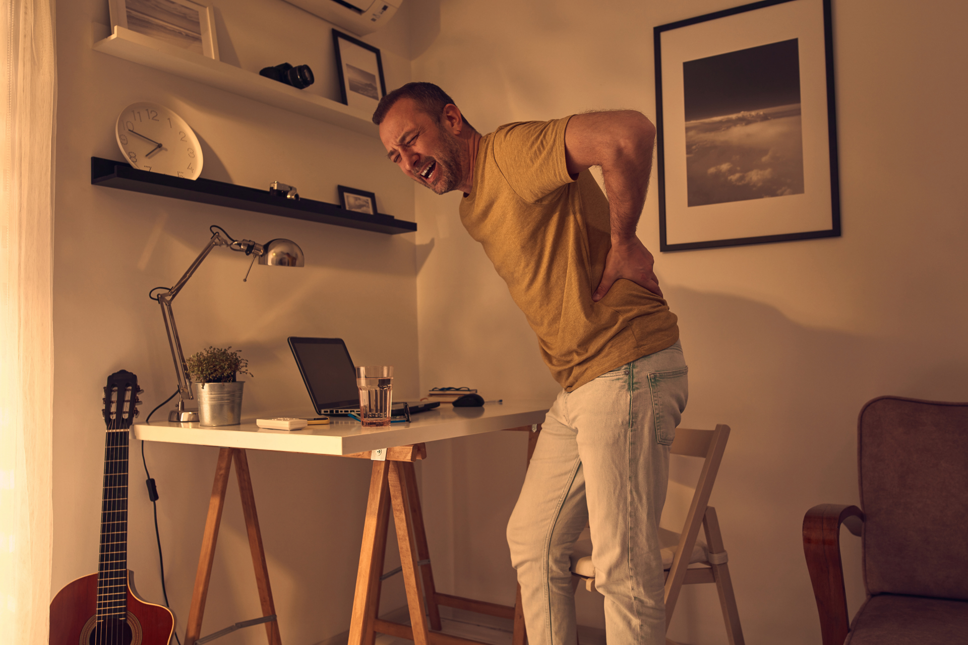 Man standing in a home office holding his lower back in severe pain