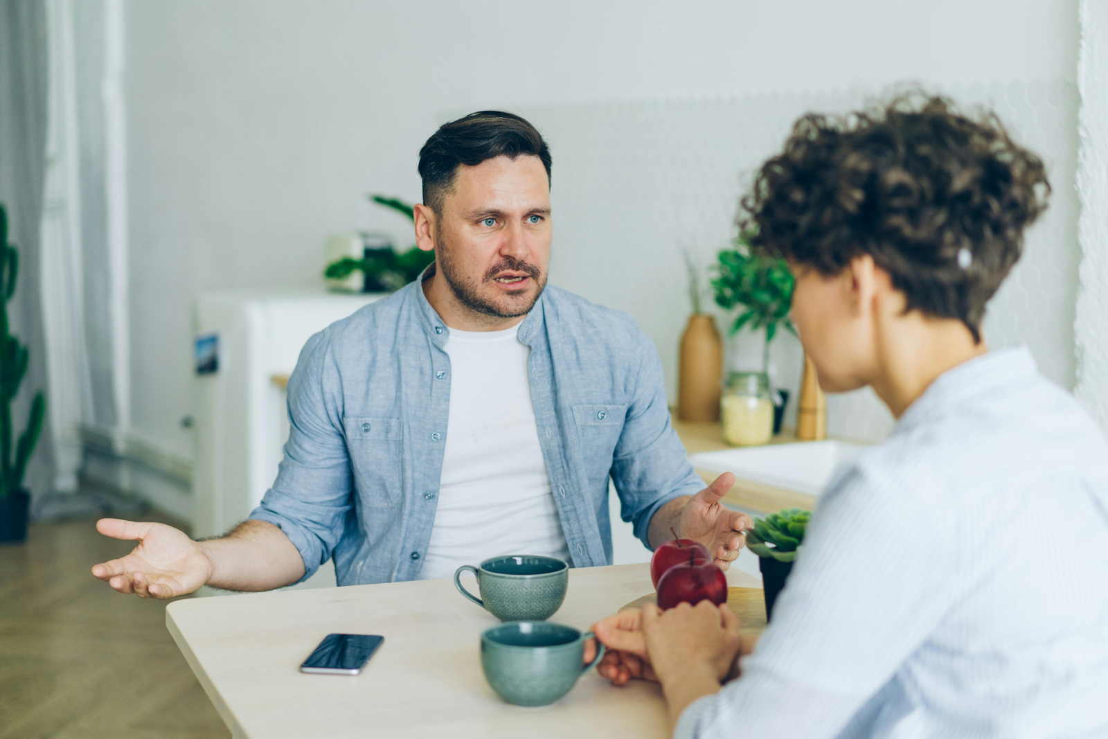 Man talking seriously with another person at a table over coffee.