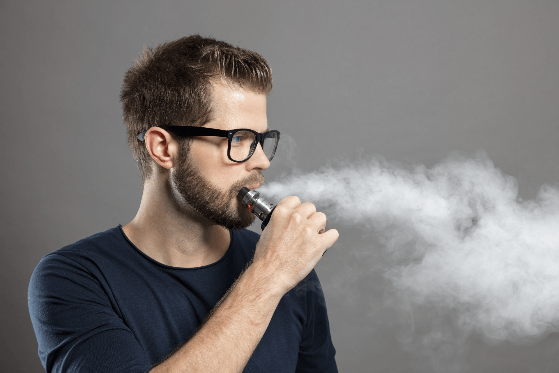 Man wearing glasses using an e-cigarette, exhaling vapor