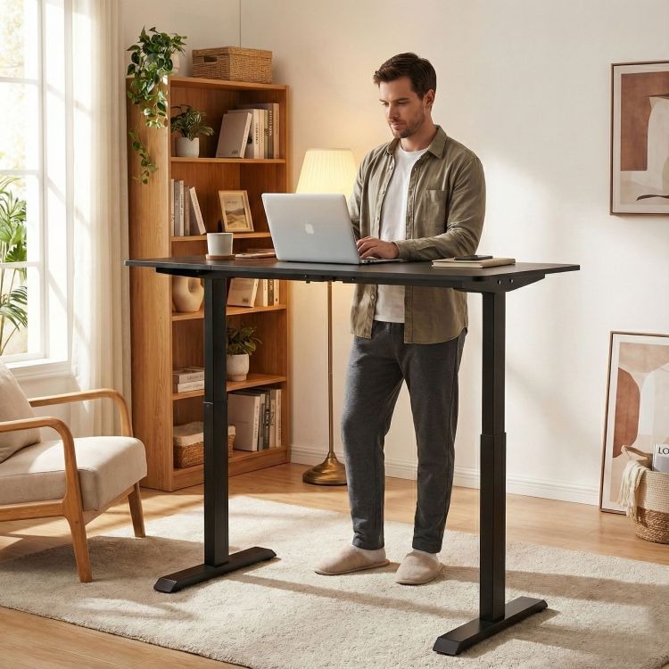 Man working on a laptop at an adjustable standing desk in a home office