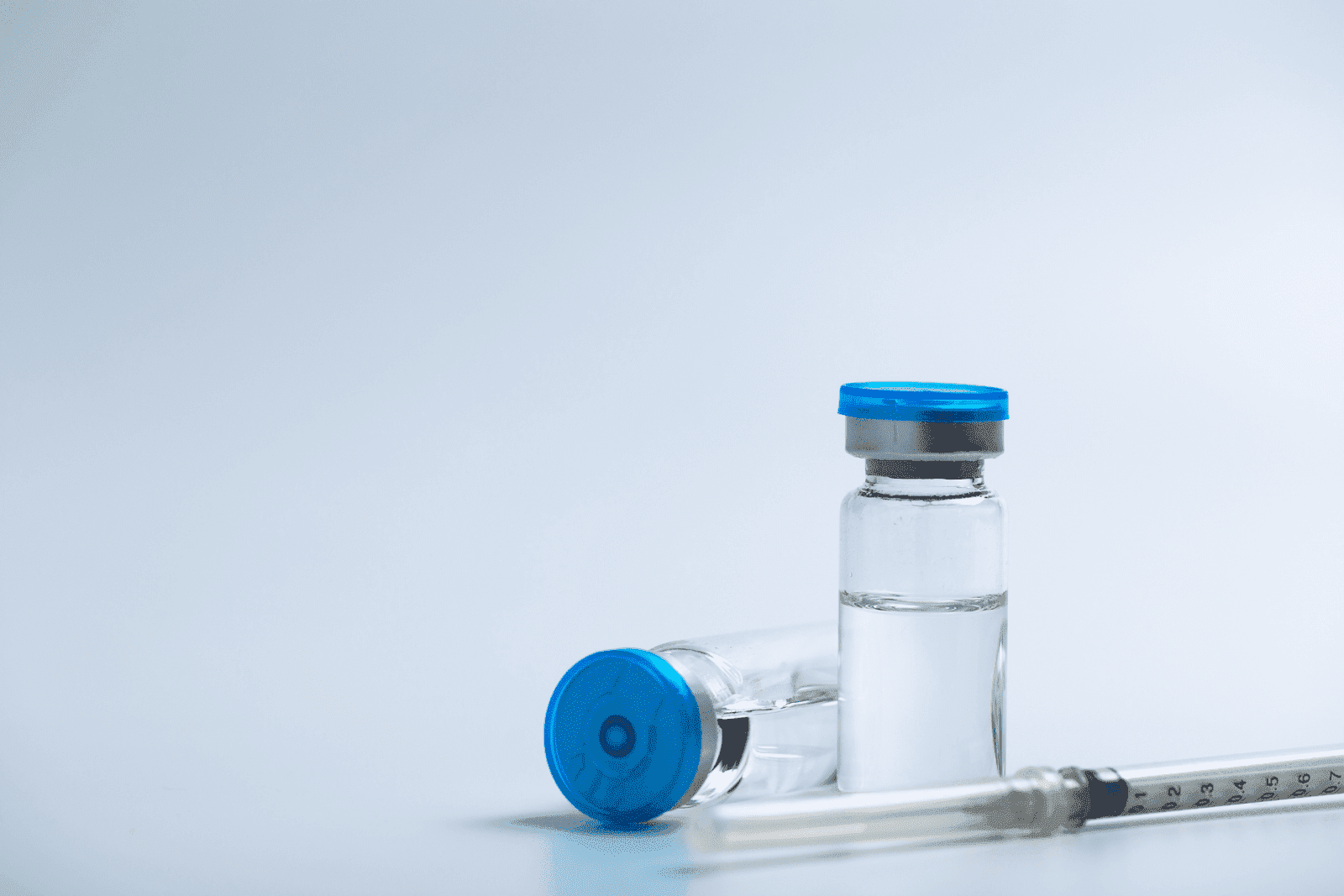 Medical vials with blue caps and a syringe on a light background