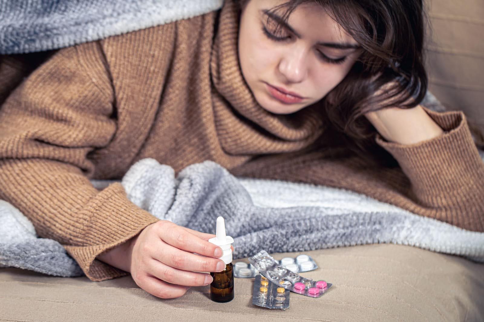 Young sick woman laying on her bed with medicine