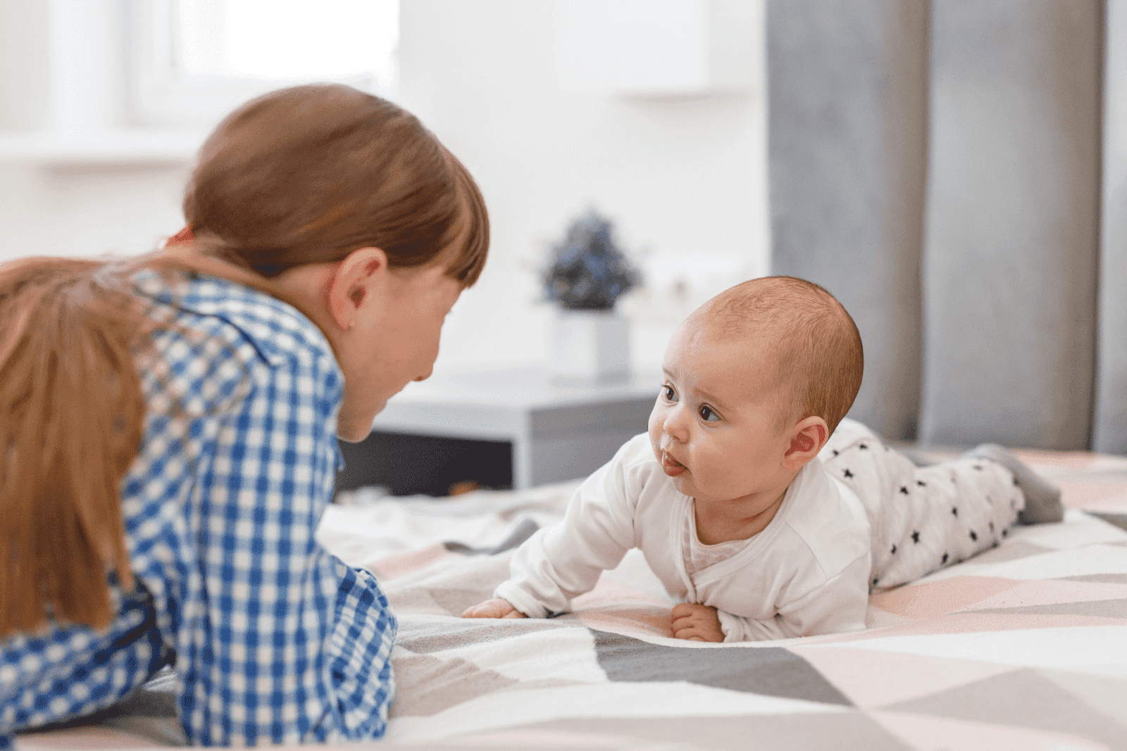 Mother and baby lying on the bed facing each other.