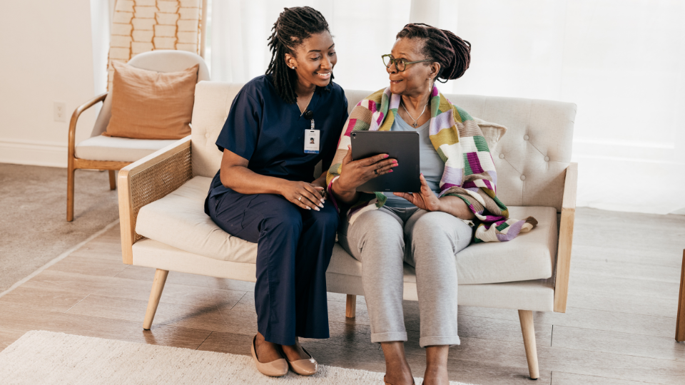 Nurse assisting patient with completing medical forms on tablet.