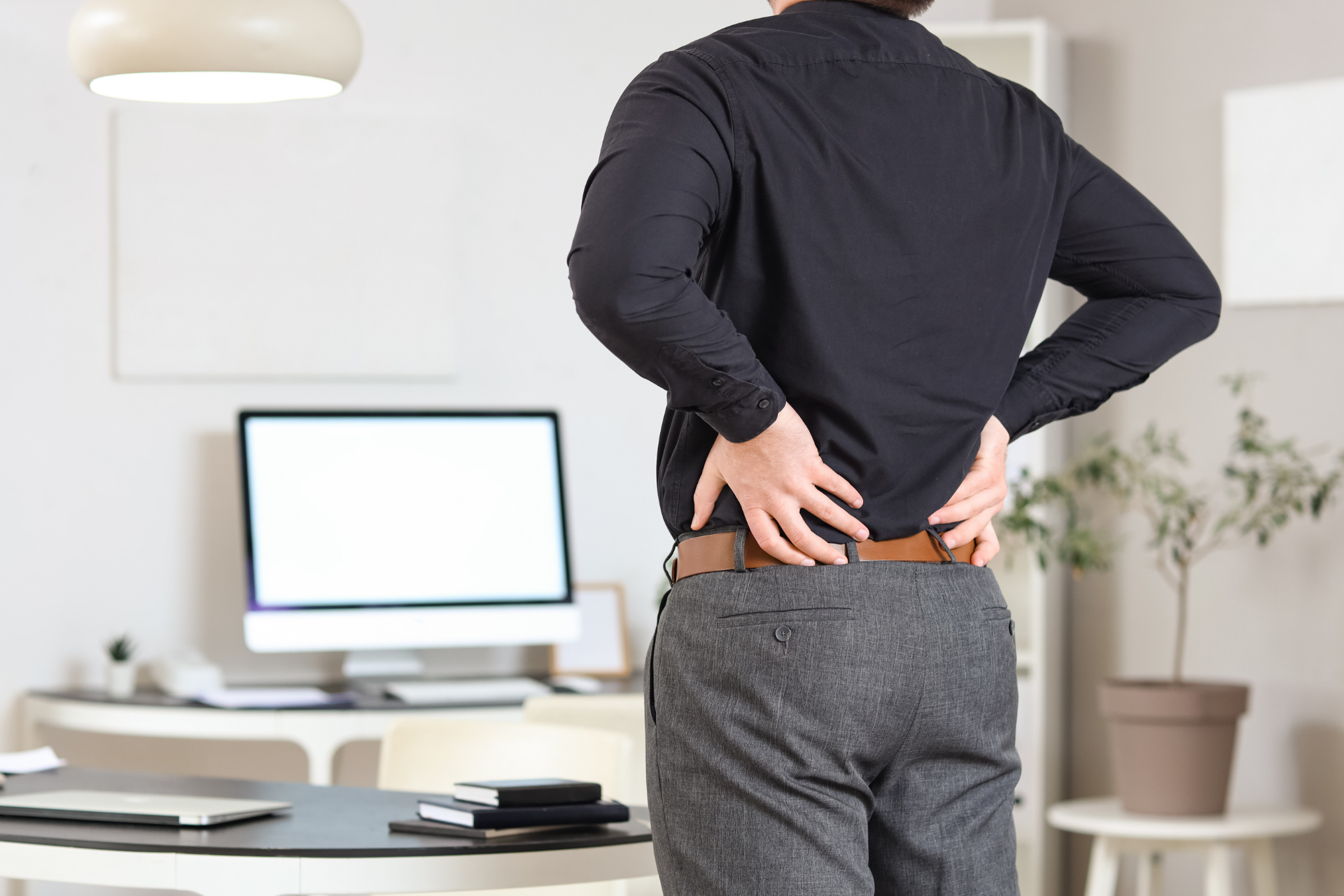 Office worker standing with hands on lower back, showing discomfort or back pain