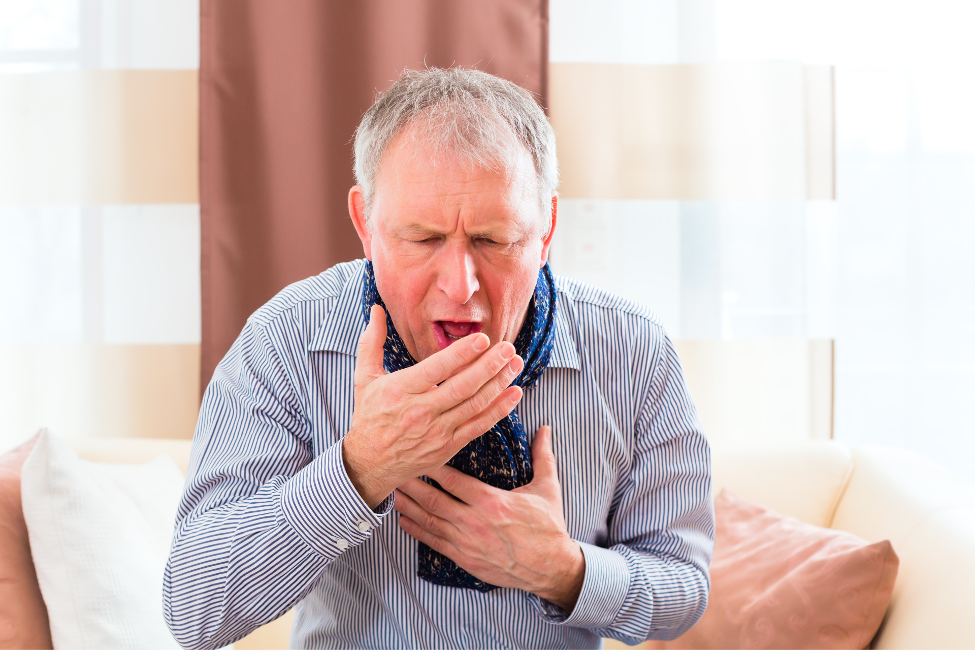 Older man coughing into his hand while holding his chest indoors