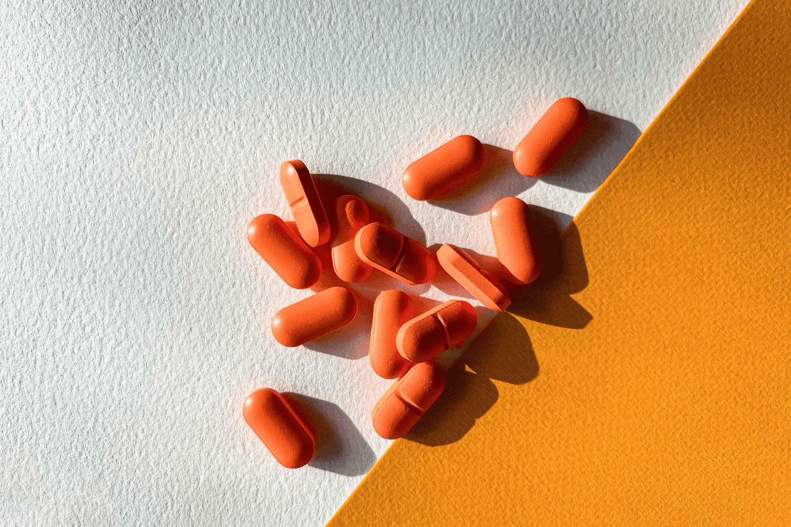 Orange tablets scattered on a two-tone white and yellow surface.