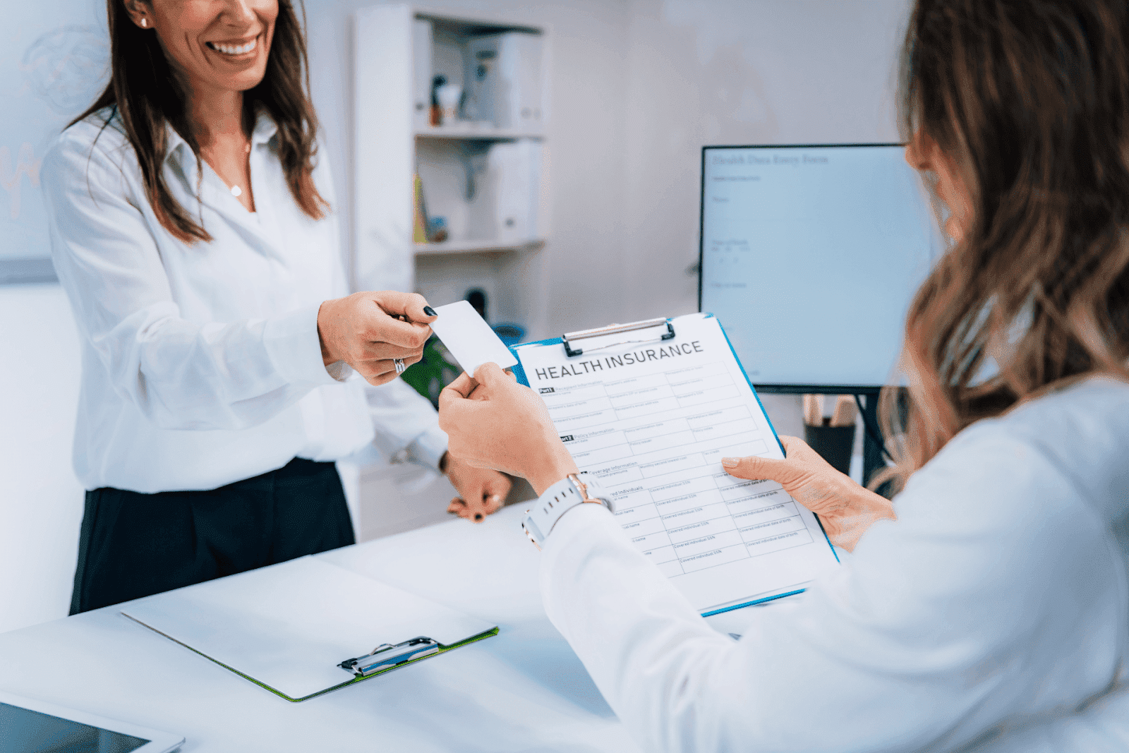 Patient handing over an insurance card to a receptionist with a health insurance form