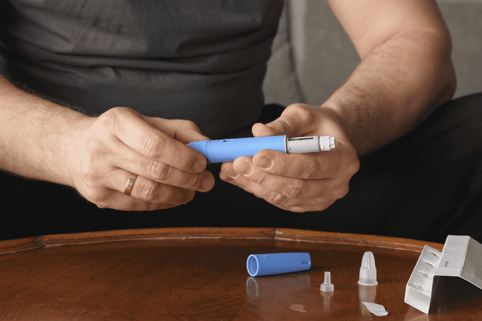 Person assembling a blue insulin pen on a table with medical supplies
