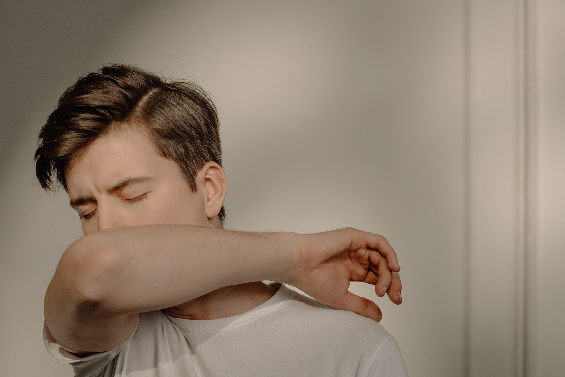 Person coughing into their elbow, practicing proper cough etiquette indoors
