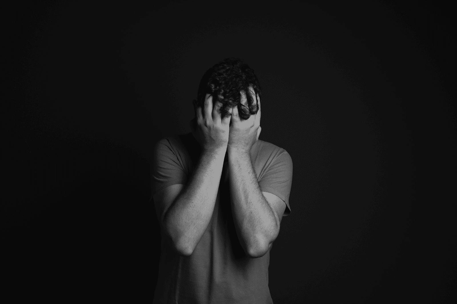 Person covering their face with hands in distress, symbolizing anxiety or depression, against a dark background.