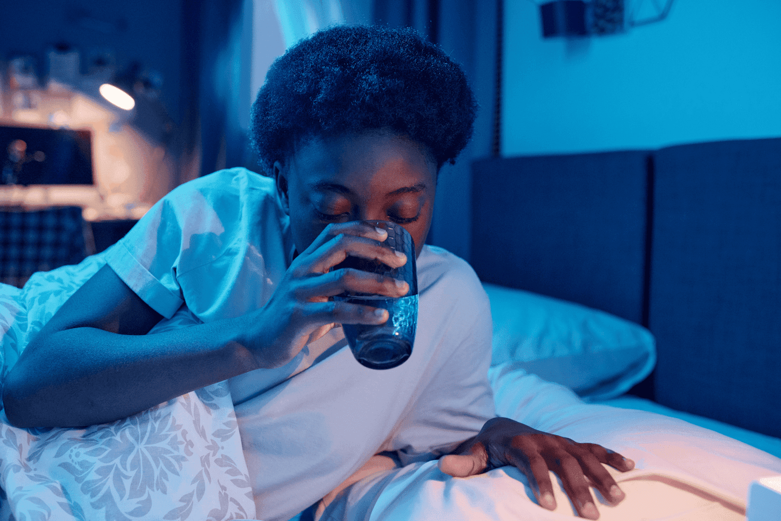 Person drinking a glass of water while sitting up in bed at night.