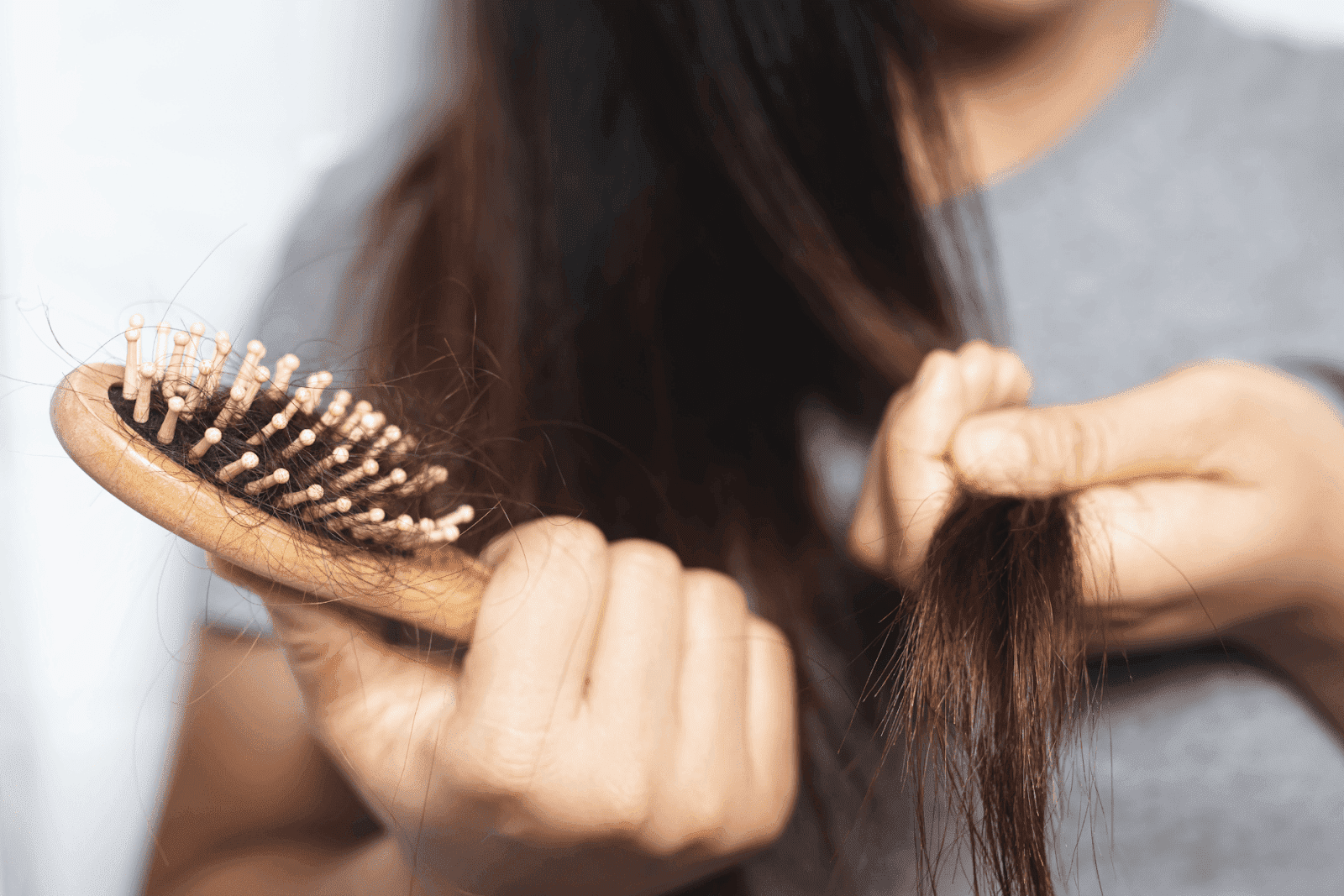 Person holding a hairbrush with strands of hair and checking their hair for hair loss