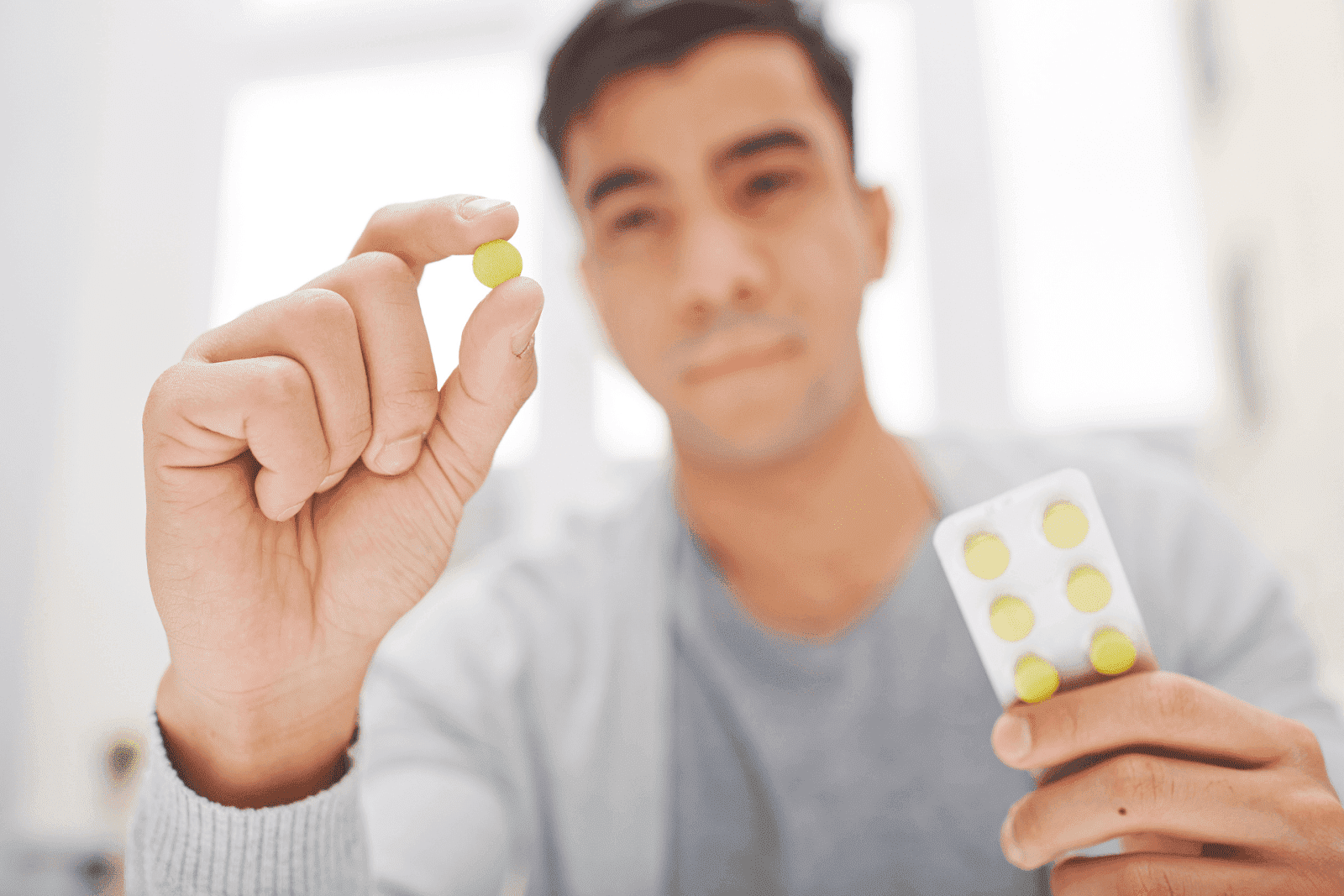 Person holding a small yellow pill and a blister pack of tablets
