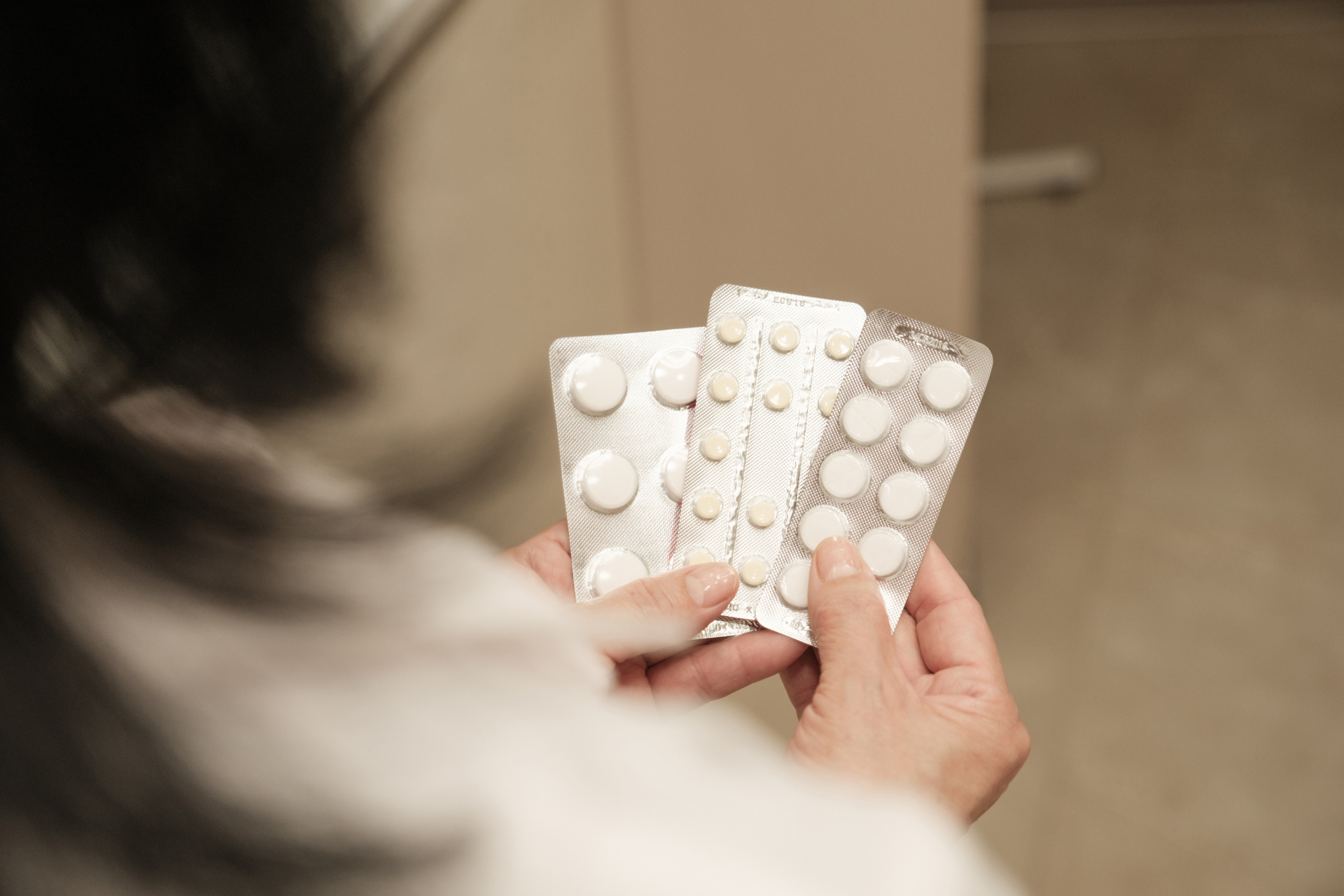 Person holding multiple blister packs of round tablets, appearing to compare or review different medications indoors