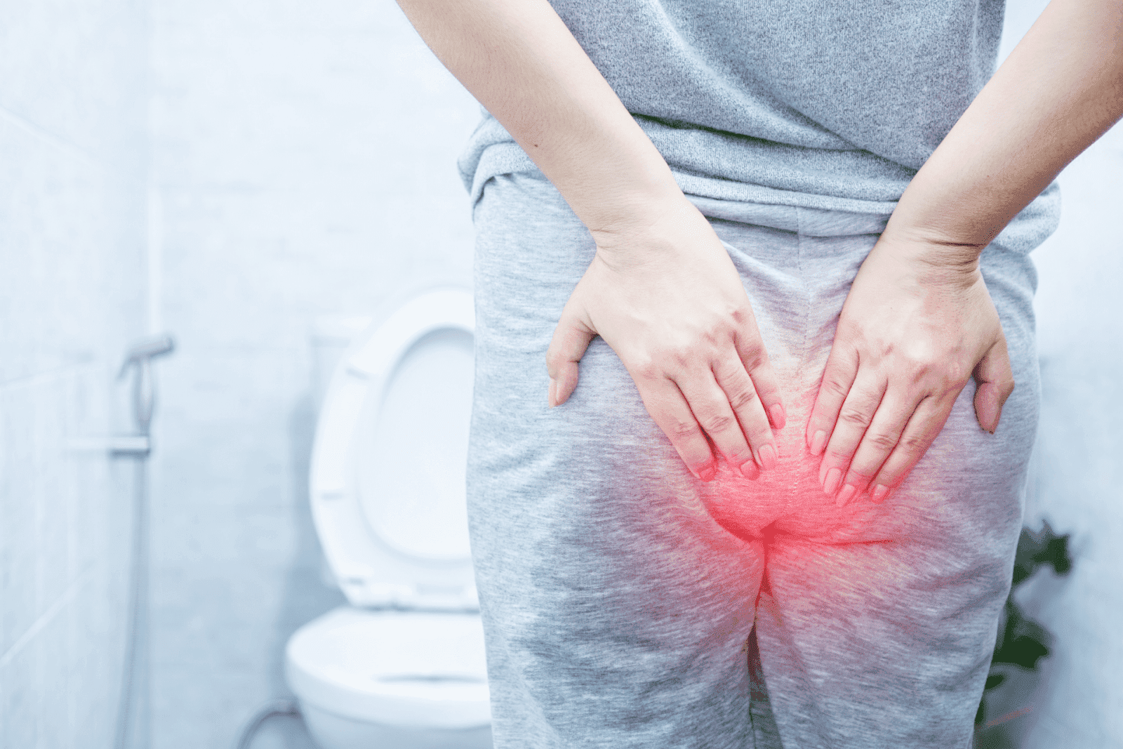 Person holding their lower back in pain with red highlight, standing in front of a toilet