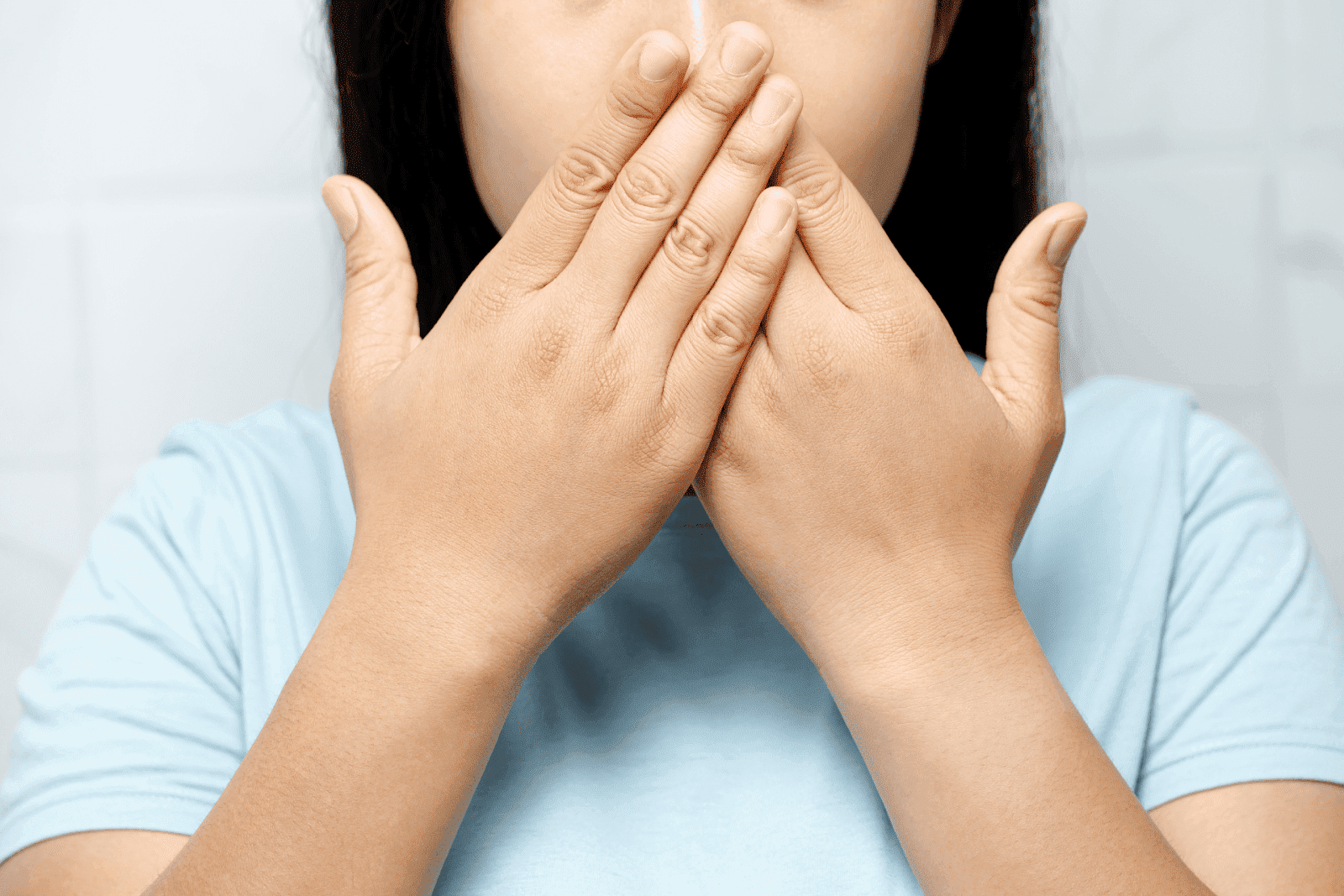 Person in a light blue shirt covering her mouth with both hands