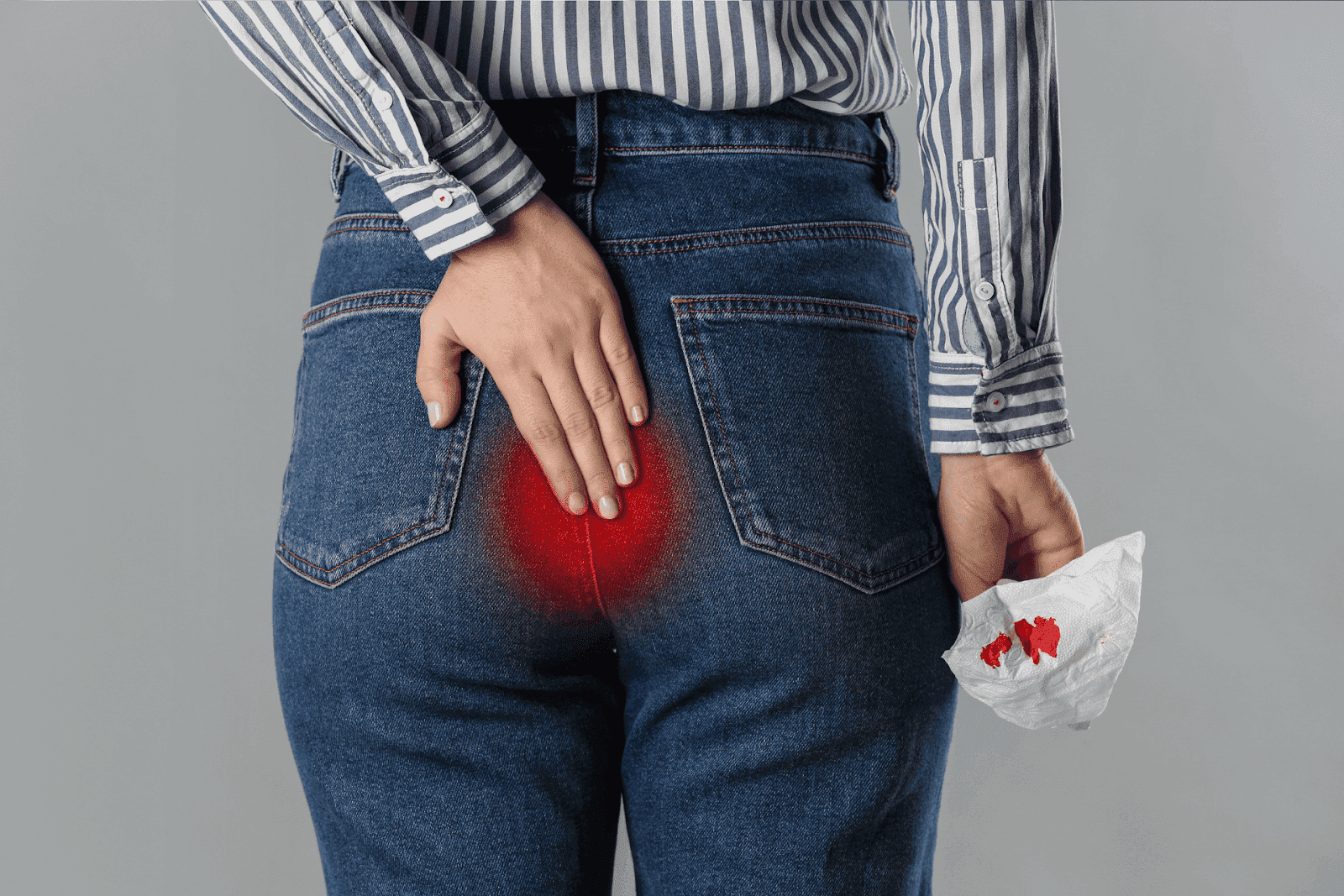 Person in jeans holding tissue with blood stains, hand on painful buttocks area