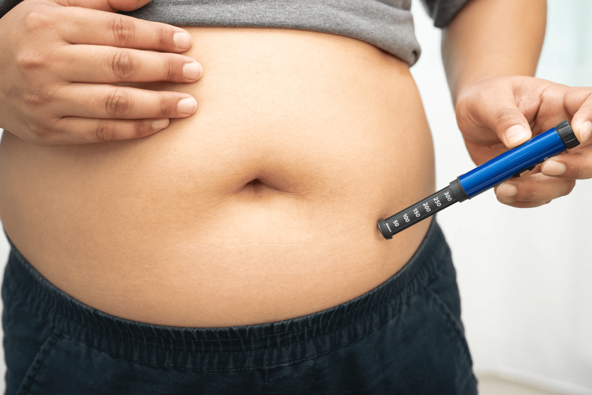 Person injecting medication into the lower abdomen with an insulin pen.
