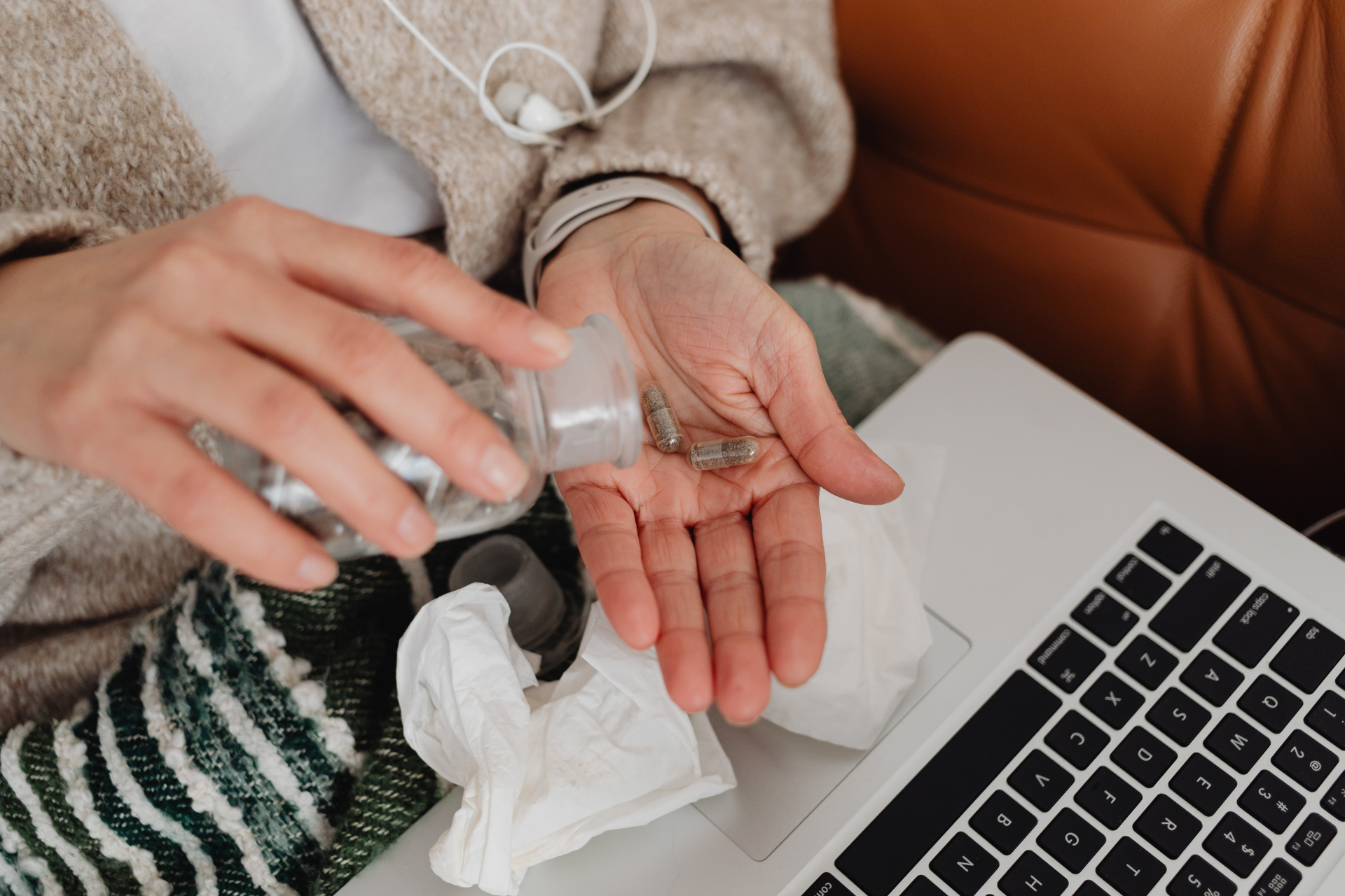 Person pouring capsules into their hand beside a laptop and tissues